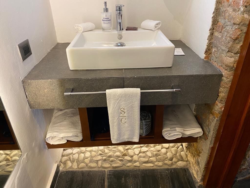 Un baño con lavamanos blanco, encimera oscura y un perchero con toallas.