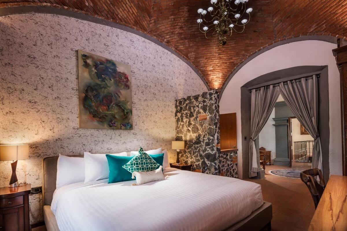 A bedroom with a large bed, a stone accent wall, a chandelier, and a painting.