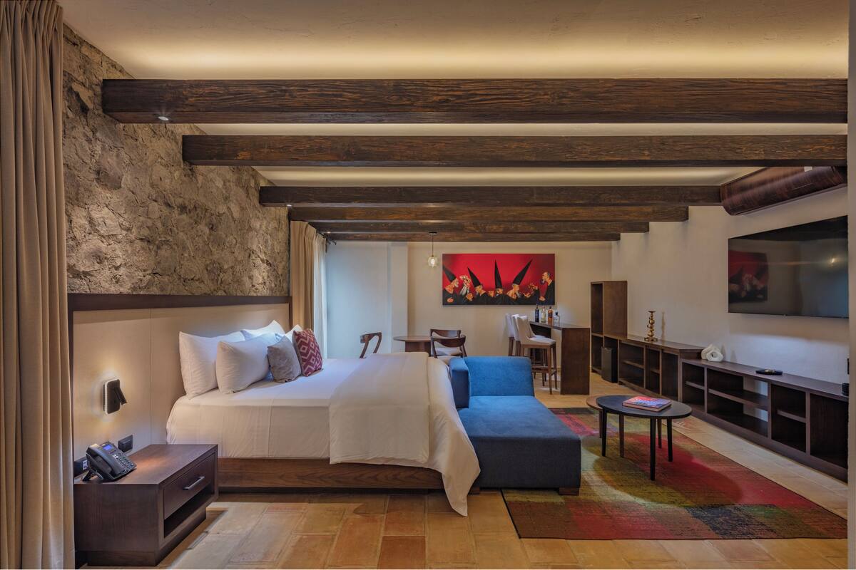 A modern hotel room with a large bed, a sofa, a TV, and a desk.