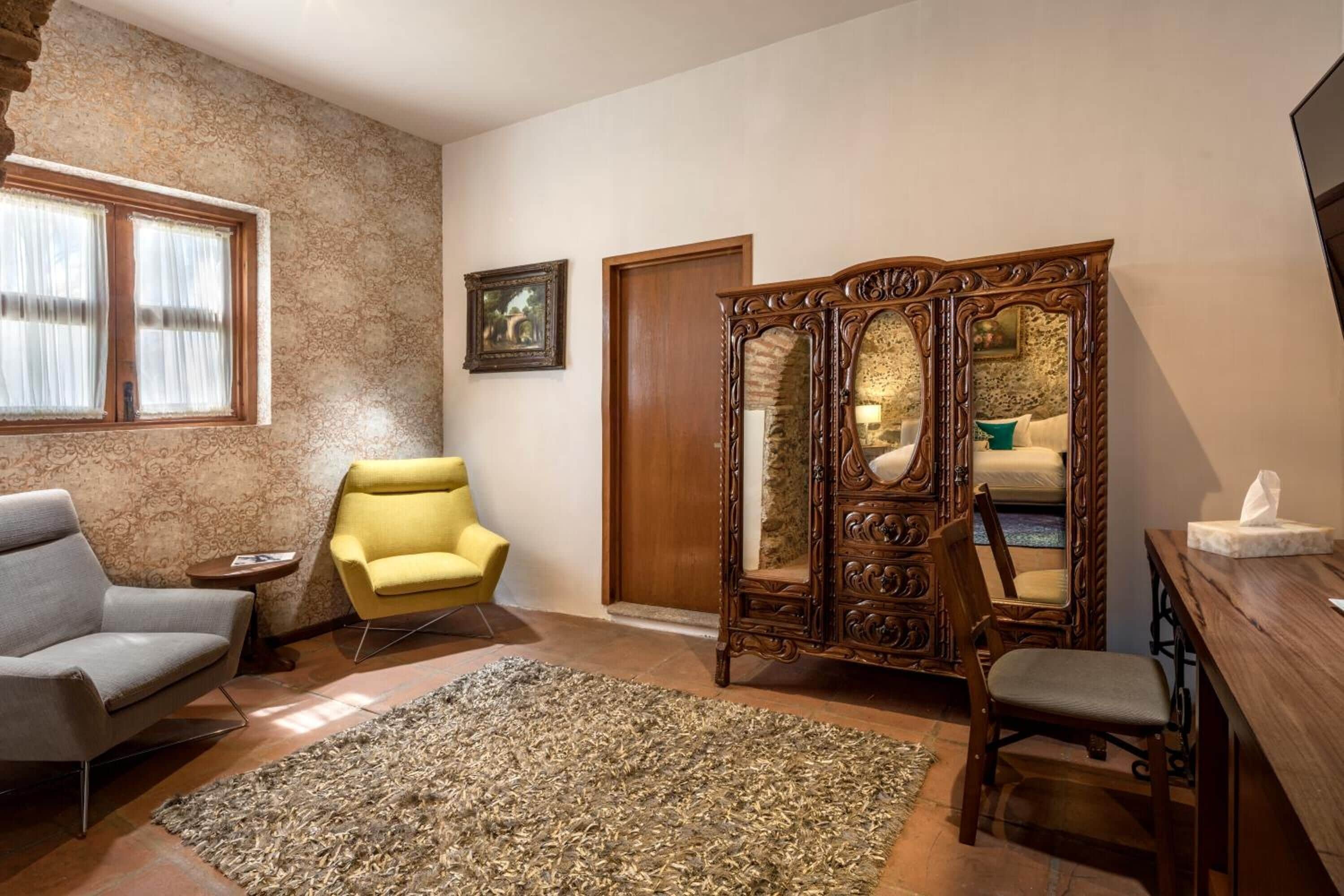 Une pièce avec un canapé gris, un fauteuil jaune, un meuble en bois avec un miroir et une petite table sur laquelle se trouve une boîte de mouchoirs.