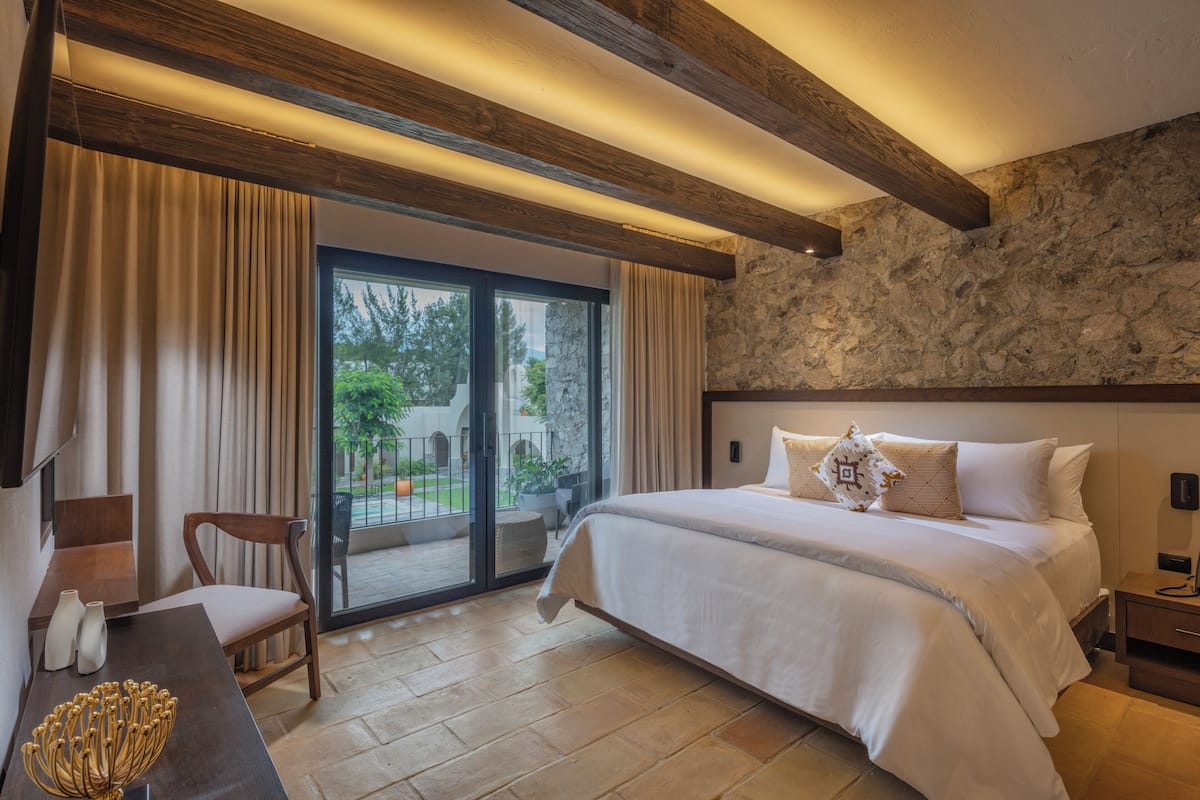 A bedroom with a large bed, a wooden ceiling, a stone wall, and a view of the outdoors.