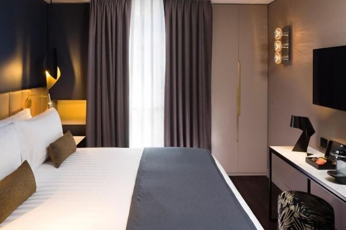 Une chambre d’hôtel avec un lit, un bureau, une chaise, une télévision et des rideaux.