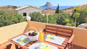 A terrace with a table set for breakfast, a view of the sea, and a mountain in the distance. - AMIBARCO-Gran Vista-Wifi y Parking Gratis. (Calpe)