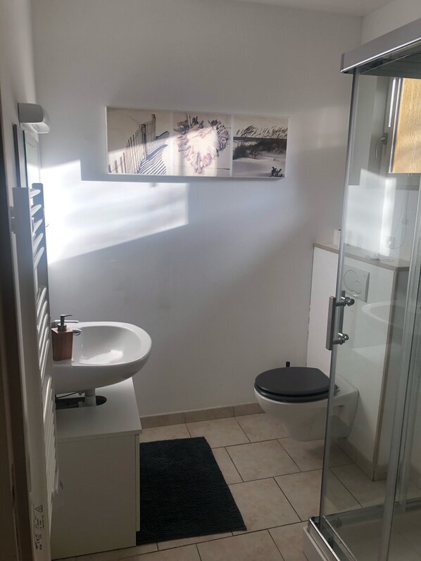 Une salle de bain moderne avec un lavabo blanc, des toilettes et une douche à parois de verre.