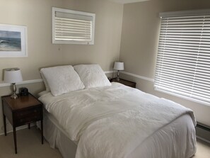 A neatly arranged bedroom with a bed, two bedside tables, a nightstand, and a window with blinds.