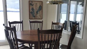 Uma sala de jantar com uma mesa e cadeiras de madeira, um lustre, uma obra de arte com um mapa na parede e grandes janelas com vista.