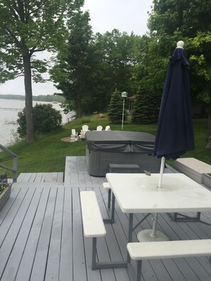 A deck with picnic tables and a hot tub, overlooking a lake.