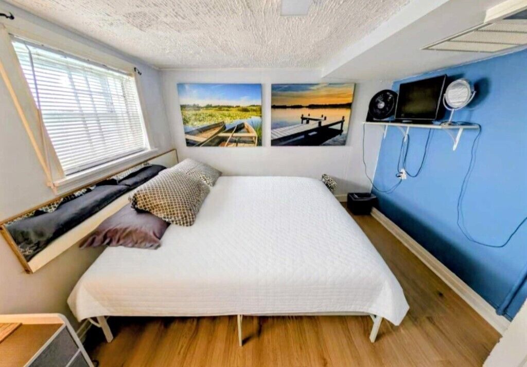 Een slaapkamer met een bed, een raam met zonwering en een kunstwerk aan de muur.