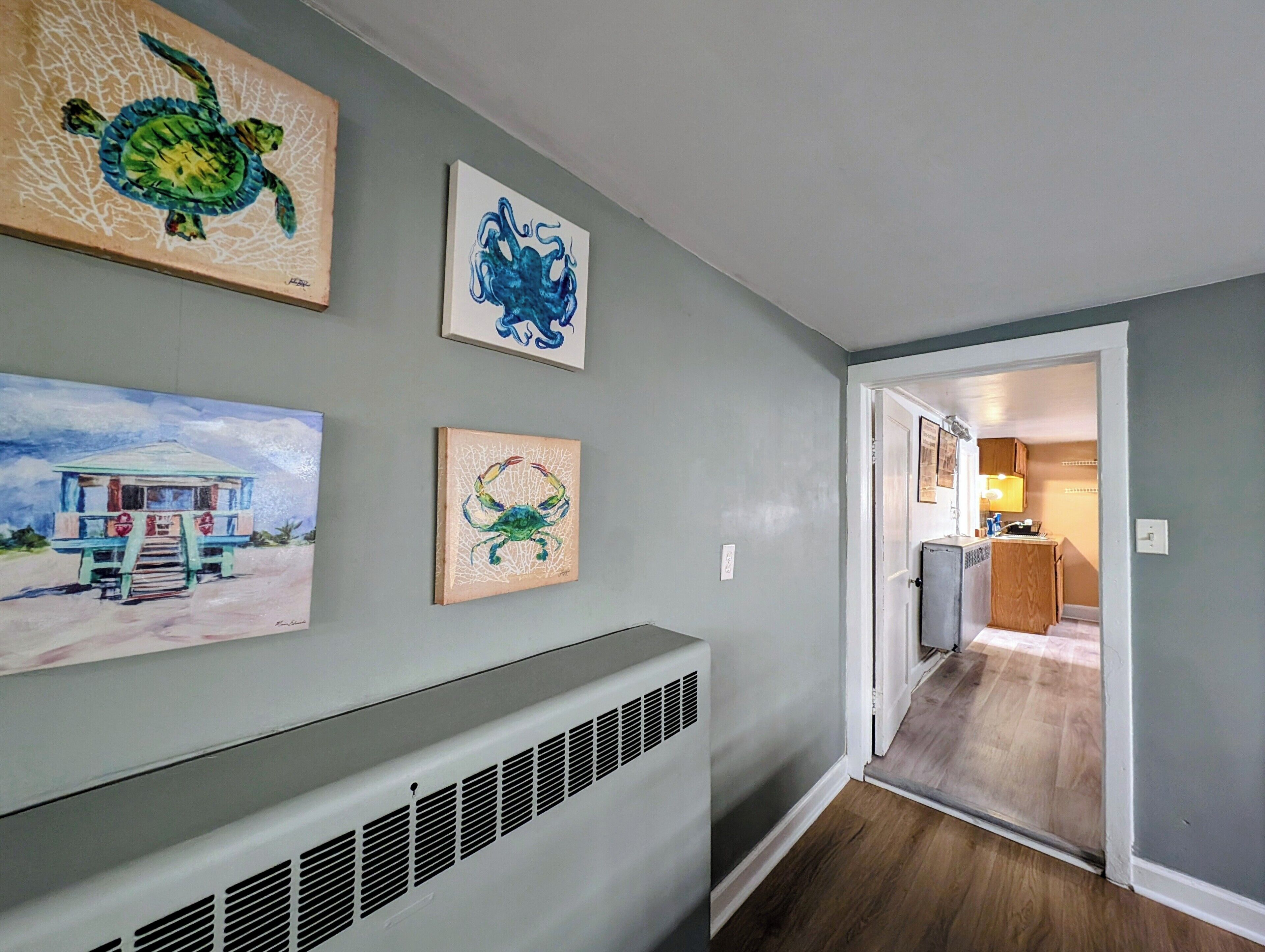 A hallway with artwork on the walls, a radiator, and a door leading to a kitchen area.