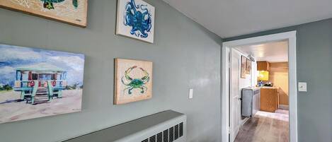 A hallway with artwork on the walls, a radiator, and a door leading to a kitchen area.