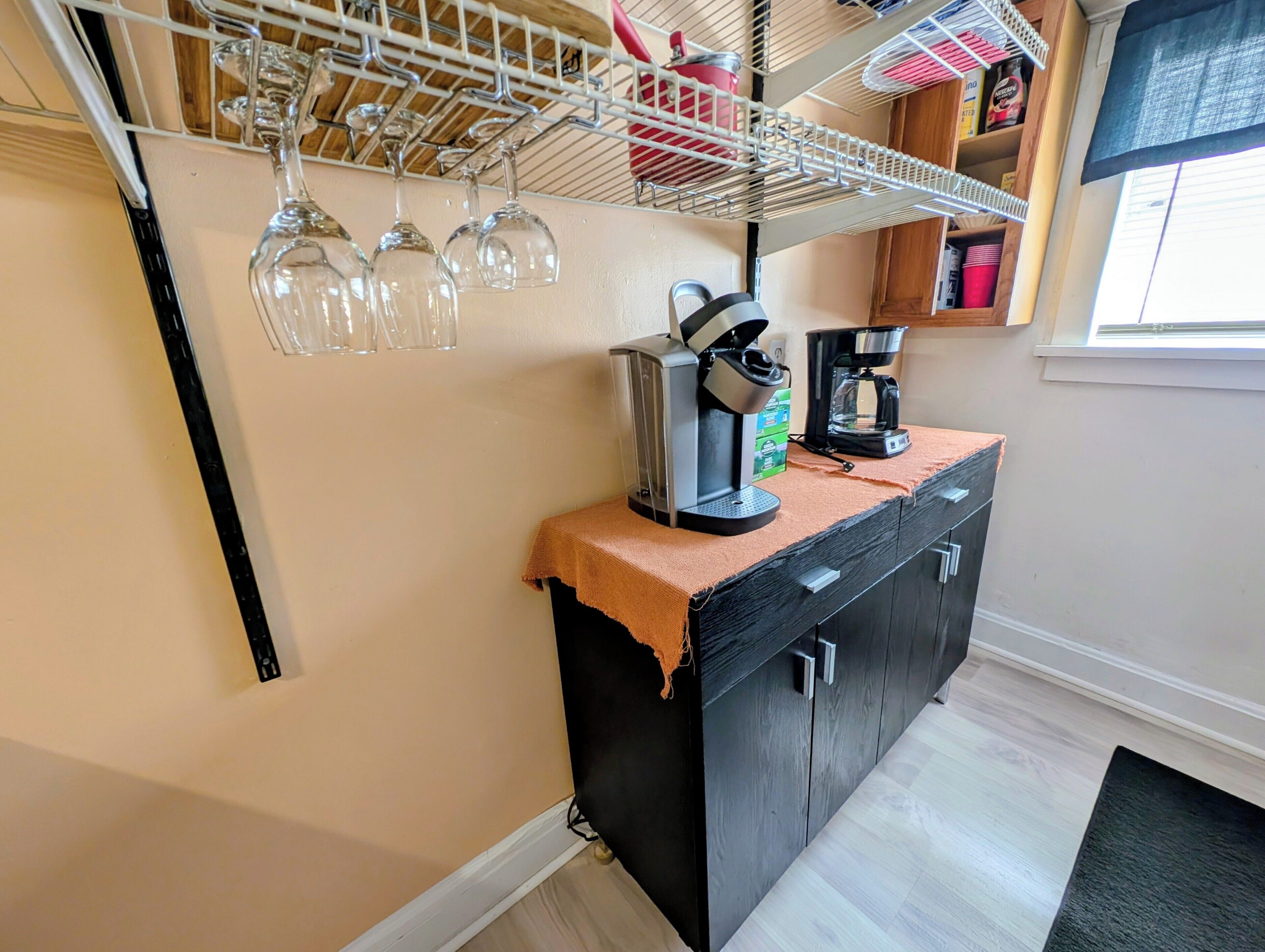 Una cocina con cafetera, copas de vino en un escurreplatos y un armario.