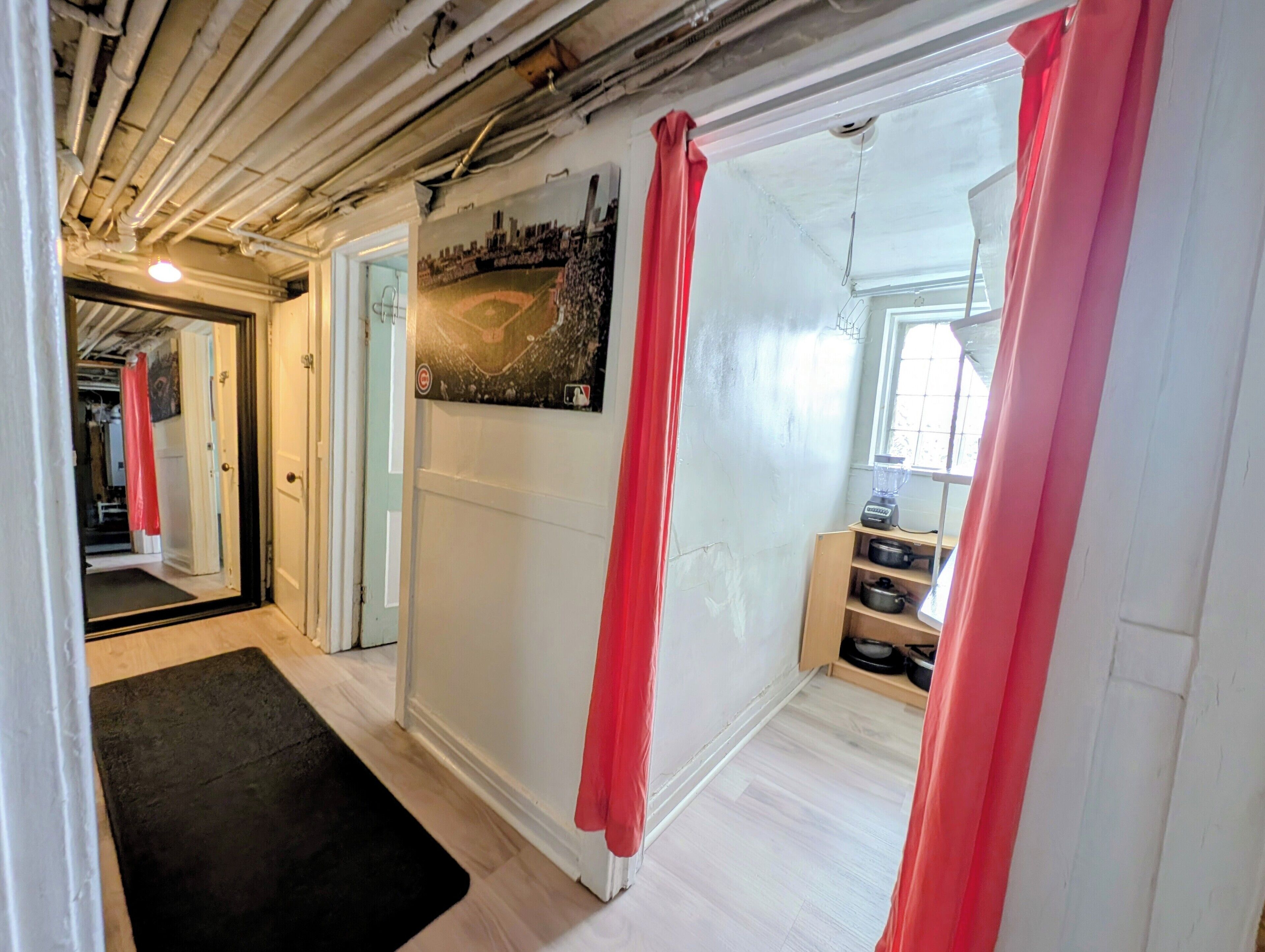 A hallway with a black mat, red curtains, a painting, and a kitchen area with pots and a blender.