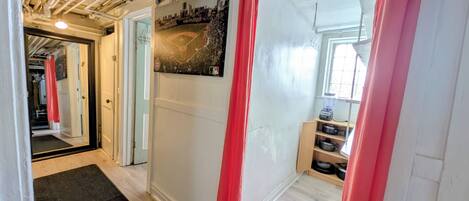 A hallway with a black mat, red curtains, a painting, and a kitchen area with pots and a blender.