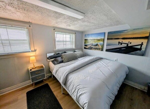 A bedroom with a bed, bedside tables, a nightstand, and two windows.