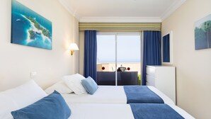 Een hotelkamer met twee bedden, een groot raam met gordijnen, een bureau met stoel, en kunstwerken aan de wanden.