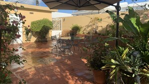A patio with a table and chairs, surrounded by potted plants and a large umbrella. - STUDIO  Walking distance to beach. (Isla Verde)