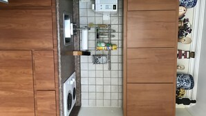 A compact kitchen with wooden cabinets, a microwave, a washing machine, and a green storage bin. - STUDIO  Walking distance to beach. (Isla Verde)