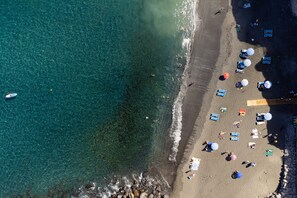 An aerial view of a beach with clear water, a rocky shoreline, and several umbrellas and lounge chairs. - LUXURY EXCLUSIVE PENTHOUSE WITH PANORAMIC VIEWS (Los Gigantes , Tenerife)