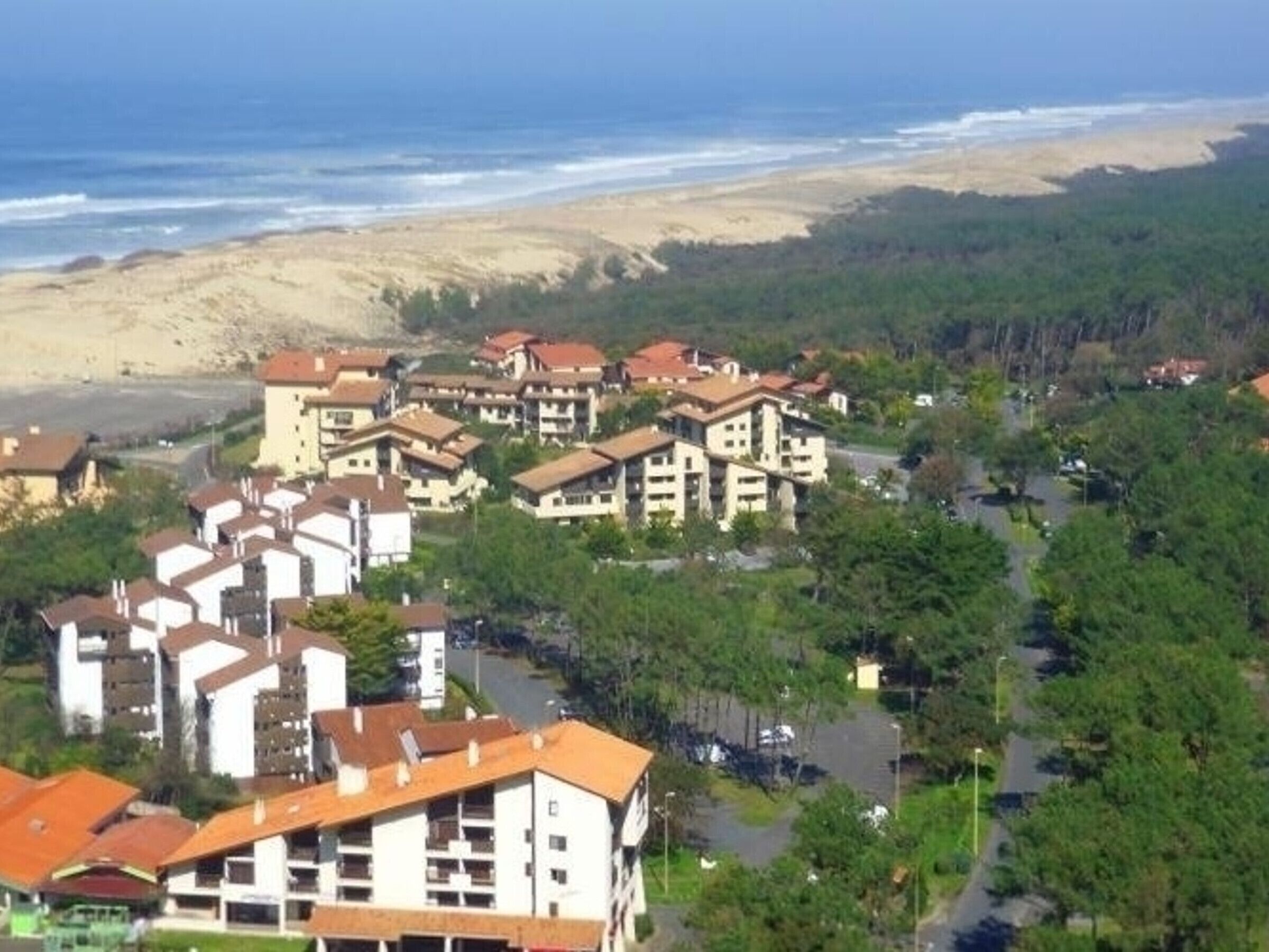 Un quartier résidentiel situé sur la côte, avec des immeubles à plusieurs étages, une plage en arrière-plan et une route qui traverse le domaine.