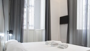 Quarto de hotel com cama, televisão de tela plana na parede e janela com cortinas.