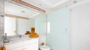 Une salle de bain moderne avec un grand miroir, un meuble-lavabo blanc et une cabine de douche en verre.