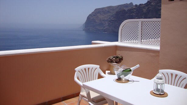Un balcon avec une table blanche, deux chaises blanches, une bouteille de champagne et une lanterne.