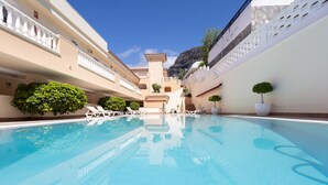 Une piscine entourée de chaises longues et de plantes en pot, le tout bordé d’immeubles beiges dotés de balcons.