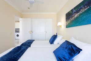 A hotel room with a large bed, a ceiling fan, a painting of a beach, and a washing machine in the background. - SUPERB LOCATION - PANORAMIC SEA & CLIFF VIEWS - WIFI - SATELLITE TV- SKY TV (Los Gigantes , Tenerife)
