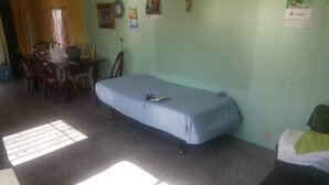 Une pièce comprenant un lit, un bureau avec un ordinateur portable, des chaises et une fenêtre avec des rideaux.