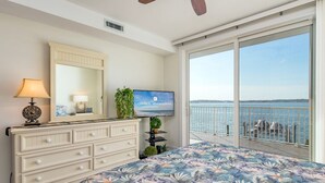 A bedroom with a large bed, a dresser, a television, and a balcony with a view of the water. - Luxury condo with amazing bay front view (Ocean City)
