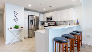A modern kitchen with white cabinets, stainless steel appliances, a central island with bar stools, and a decorative wall piece. - Luxury condo with amazing bay front view (Ocean City)
