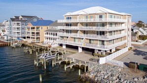 A multi-story waterfront hotel with balconies, a dock, and a rocky shoreline. - Luxury condo with amazing bay front view (Ocean City)