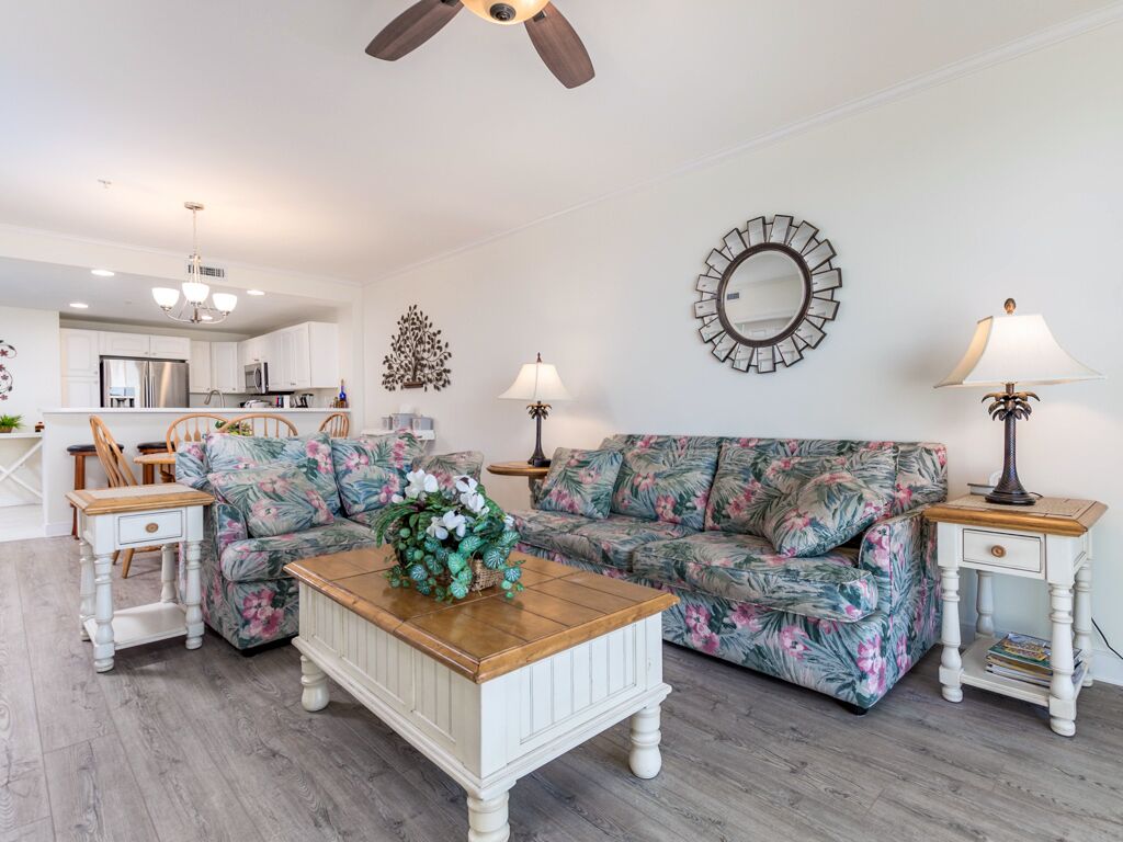 A living room with a sofa, coffee table, and two side tables. There is a kitchen in the background.