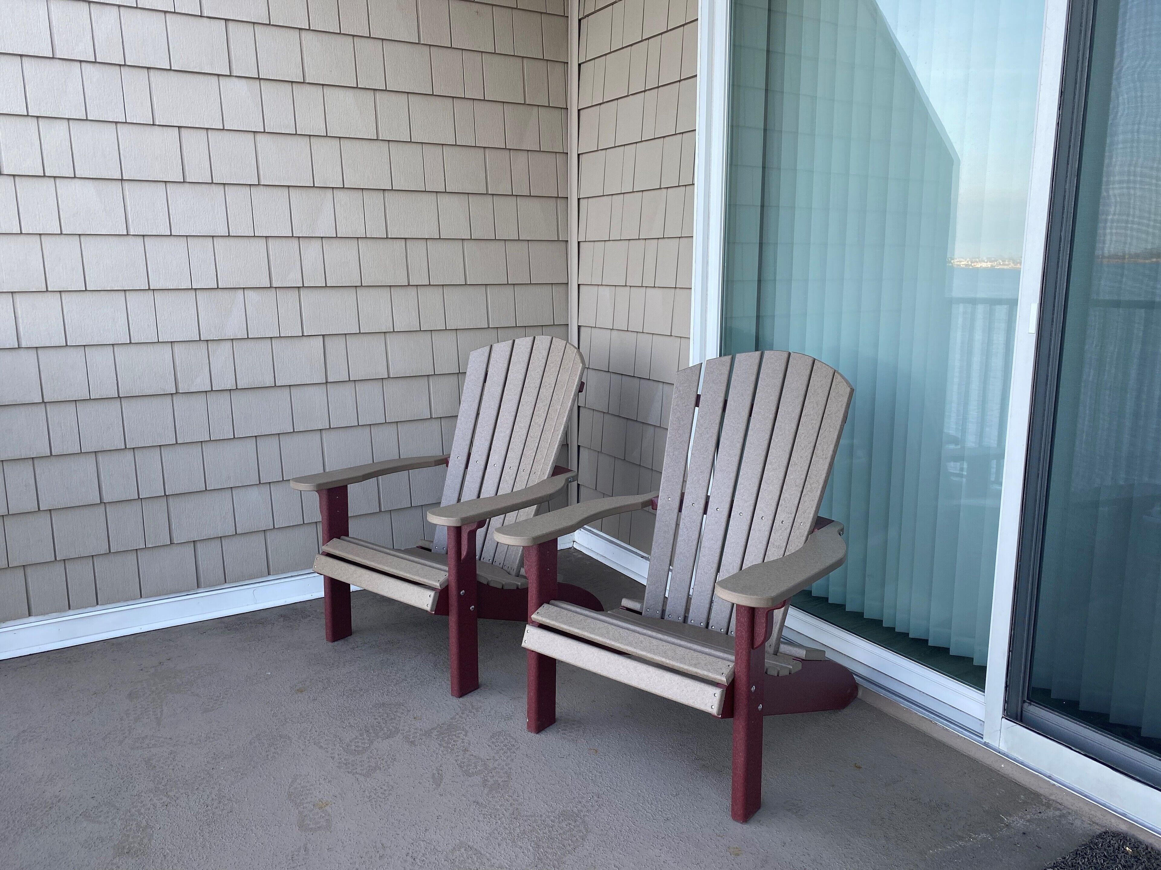 Et sæt Adirondack-stole på en beton terrasse med en beige facade af skifer og en glasdør.