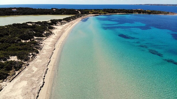 Eine Luftaufnahme einer Küstenlandschaft mit einem Sandstrand, klarem, blauem Wasser und einer entfernten Küstenlinie.