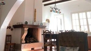 Ein geräumiges Wohnzimmer mit hoher Decke, freiliegenden Holzbalken, einem Kamin und einem Essbereich mit Holztisch und -stühlen.