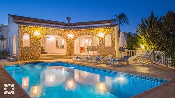Une villa avec piscine, dotée d’une façade en pierre, d’une piscine et de chaises longues.