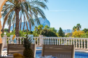 Un espace aménagé au bord de la piscine, offrant une vue sur une montagne et des palmiers.