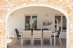 An outdoor patio with a stone archway, a table with chairs, and a decorative wall piece.