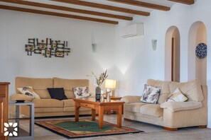 A living room with two sofas, a coffee table, and a rug. There is a wall-mounted air conditioner and a decorative wall piece.