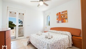 Une chambre à coucher avec un lit, un ventilateur de plafond, une fenêtre et un tableau accroché au mur.