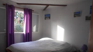 Ein Schlafzimmer mit einem Einzelbett, violetten Vorhängen, einem Fenster und einem kleinen Nachttisch mit einer Lampe.
