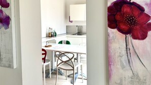 A dining area with a white table and chairs, a kitchen in the background, and a painting of red flowers on the wall. - S023 - Sirolo, magnificent design three-room apartment with terrace (Sirolo)