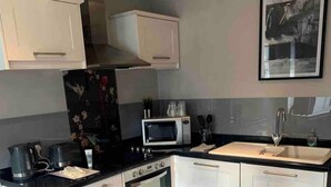 Une cuisine de taille réduite, avec des meubles blancs, un four à micro-ondes, une cuisinière et un évier.