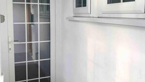 Une porte blanche avec un panneau de verre, une petite fenêtre au-dessus, et une marche sombre menant à la porte.