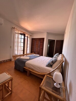Une chambre à coucher avec un lit, une table de chevet, une chaise et une fenêtre avec des rideaux.
