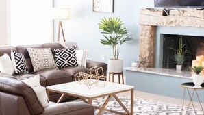 Un salon avec un canapé en cuir marron, des coussins à motifs, une table basse blanche et une cheminée.