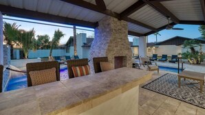 Un espace bar extérieur agrémenté de piliers en pierre, de mobilier en osier et d’une piscine.
