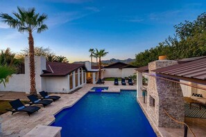 A swimming pool with lounge chairs, palm trees, and a stone building with a tiled roof. - Private Pool with Waterslide & Movie Theater (Scottsdale)
