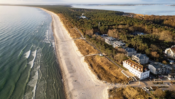 Vista aérea de una zona costera con playa, edificios y terreno boscoso.